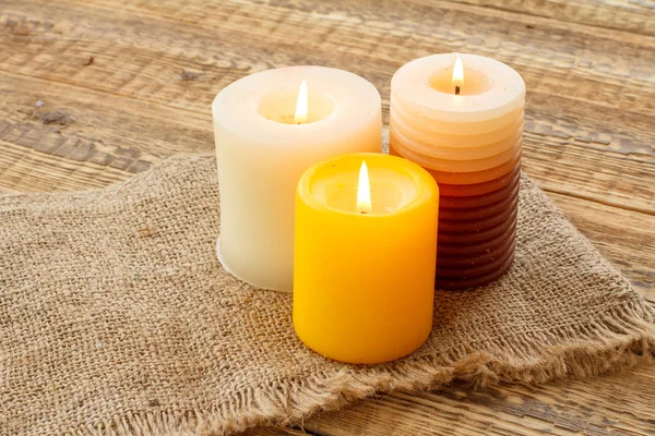 Velas ardientes sobre tela de saco y fondo de madera . — Foto de Stock