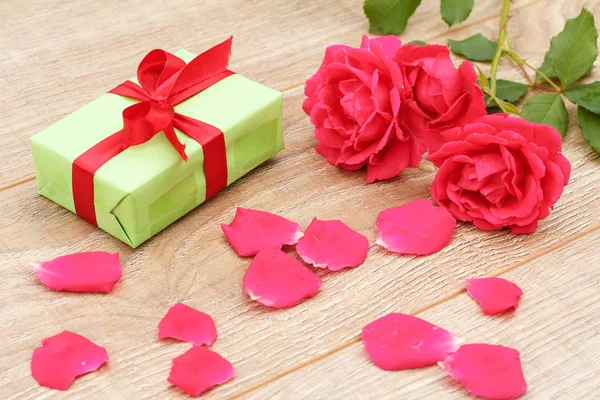 Gift box with rose flowers on the wooden background.