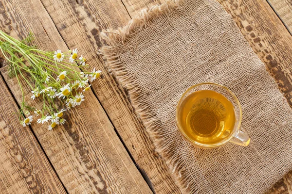 Coupe en verre de thé vert avec des fleurs de camomille blanche sur de vieux planches . — Photo