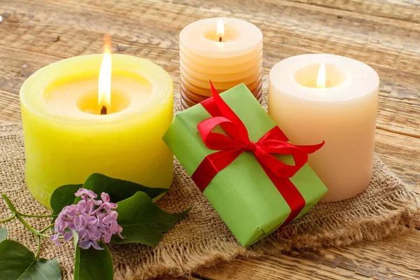 Burning candles and gift box on sackcloth and wooden background.