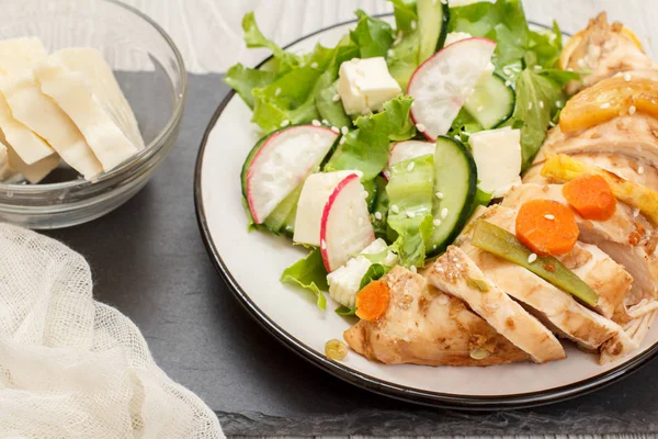 Plato con carne, ensalada de verduras con queso, pepino y rábano sobre tabla de piedra . — Foto de Stock