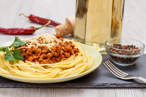 Spaghetti bolognese on a plate, spices and a bottle of wine.