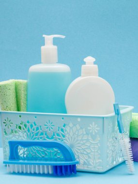 Sepette bulaşık sıvısı şişeleri, mavi arka planda sünger ler ve fırçalar.