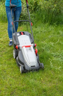 Kadın bahçede çim biçme makinesi ile çalışıyor