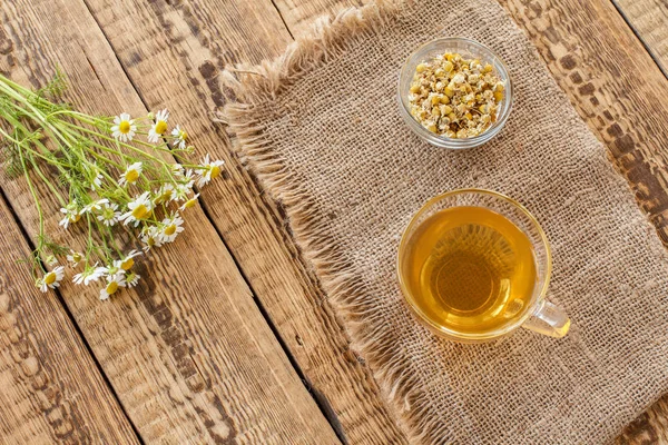 Tasse en verre de thé vert avec des fleurs de camomille sèche dans un bol . — Photo