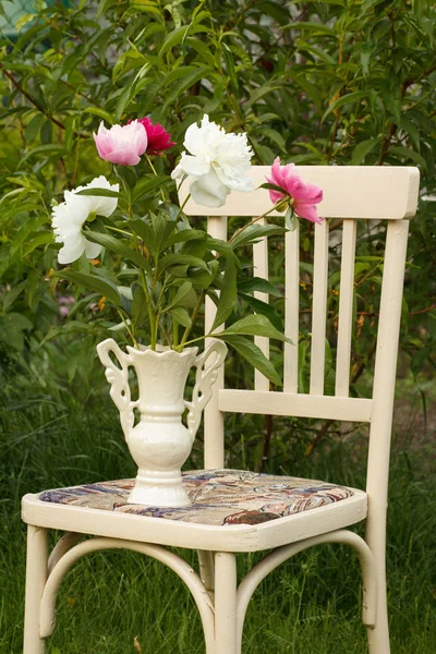 Vase of flowers on a white chair in the garden.