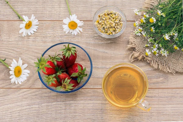 Coupe en verre de thé vert, fraises avec des fleurs de camomille blanche sur fond en bois . — Photo