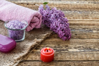 Yağ şişesi, deniz tuzu, sabun, mum ve ahşap zemin üzerinde leylak çiçekleri olan havlu..