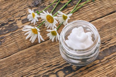Kozmetik krem ve ahşap arka planda taze papatya çiçeği..