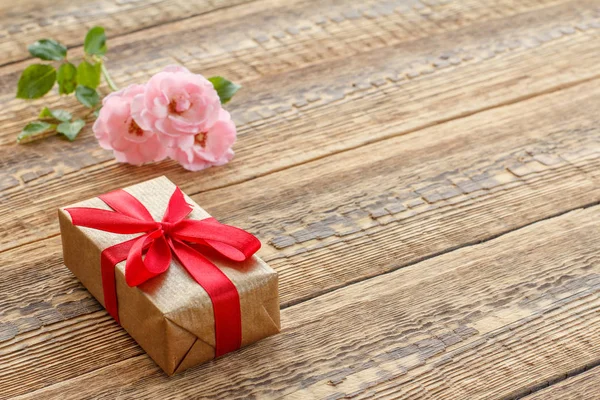 Dárková krabička na dřevěných prknech s růžovými květy — Stock fotografie