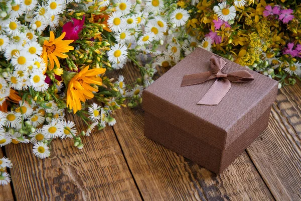 Blumenstrauß und Geschenkbox auf altem Holzbrett. — Stockfoto