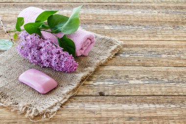 Ahşap arka planda leylak çiçekli sabun ve havlu..
