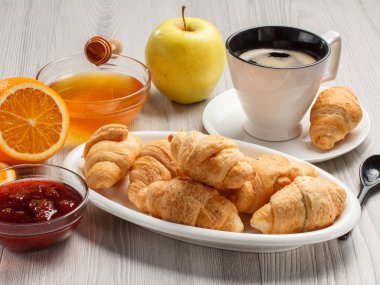 Bir fincan sade kahve, çay tabağı ve beyaz porselen tabakta taze kruvasan.