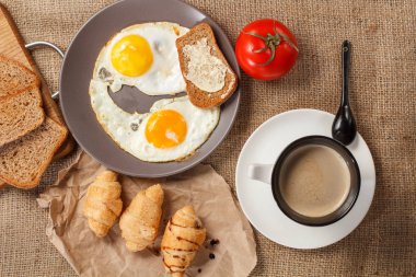 Yumurtalı tabak, bir fincan sade kahve, kruvasan ve ekmek.