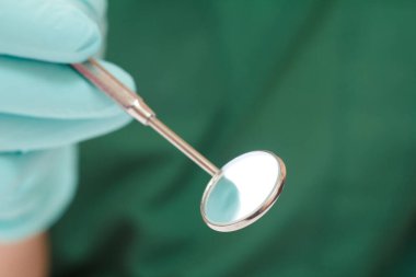 Ağız aynası ve arka planda bulanık diş hekimi eli..