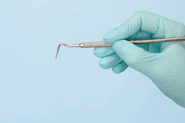 Dentist\'s hand with probe on blue background.