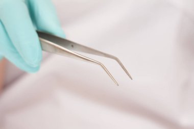 Bulanık arka planda cımbızla dişçi eli..