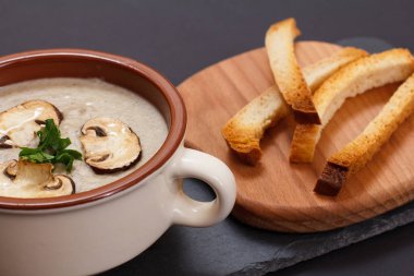 Siyah arka planda porselen kasede mantarlı krema çorbası..