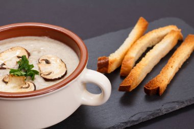 Siyah arka planda porselen kasede mantarlı krema çorbası..