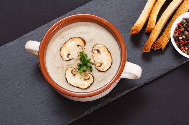 Siyah arka planda porselen kasede mantarlı krema çorbası..