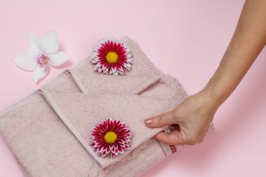 Yumuşak terli havlular ve pembe arka planda orkide ve kasımpatı olan bir kadın eli. Üst görünüm.