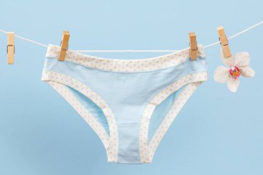 Çamaşır ipinde çamaşır mandalları ve mavi arka planda orkide çiçekli yeni pamuk külotlar. Kadın iç çamaşırı.