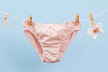 Çamaşır ipinde yeni pembe pamuk külotlar, mandallar ve mavi arka planda orkide çiçekleri. Kadın iç çamaşırı.