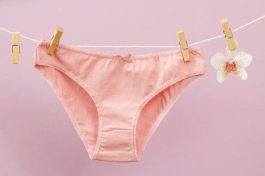 Çamaşır ipinde yeni pembe külotlar, mandallar ve leylak arka planda orkide çiçekleri. Kadın iç çamaşırı.