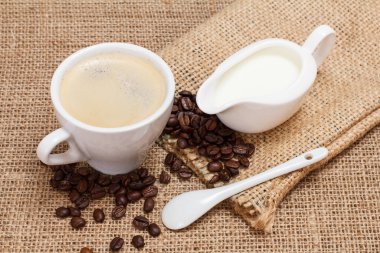 Bir fincan kahve, krema sosu, kaşık, kahve çekirdeği ve çuval bezi. Üst görünüm.