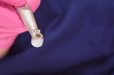 Pembe lateks eldivenli, yakın plan dişçi eli. Arka planda yüksek hızlı diş teli var. Tıbbi aletler konsepti. Sığ alan derinliği.