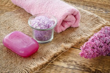 Banyo işlemleri için deniz tuzu, sabun ve havluyla dolu cam kase çuval bezi ve leylak çiçekli ahşap tahtalar. Spa ürünleri ve aksesuarlar. Üst görünüm.