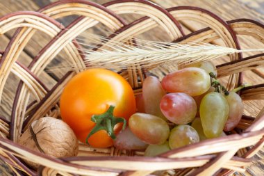 Yakın plan ceviz, domates, üzüm ve buğday kulak hasır sepetin içinde eski tahta tahtalarda. Yüzeyin derinliği. Üst görünüm.