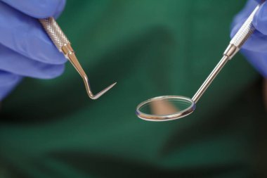 Diş hekiminin ellerinin plastik eldivenli ve ağız aynalı yakın görüntüsü. Yüzeyin derinliği. Tıbbi araçlar konsepti.