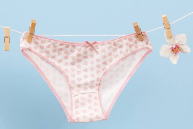 Çamaşır ipinde çamaşır mandalları ve mavi arka planda orkide çiçekli yeni beyaz pamuk külotlar. Kadın iç çamaşırı.