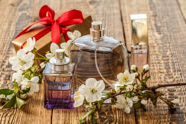 Gift box and bottles of perfume with flowering branch of jasmine on the wooden background. Concept of giving a gift on holidays.