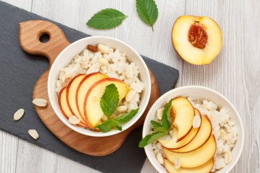 Şeftalili yulaf lapası, porselen kaselerde kaju fıstığı ve badem, ahşap tahtalarda taze şeftali. Meyveli vegan glütensiz sorghum salatası. Üst görünüm.