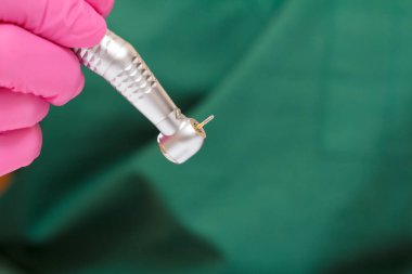 Pembe lateks eldivenli bir dişçi eli ve arka planında da yeni bir diş fırçası ve bulanık yeşil tıbbi önlük var. Tıbbi araçlar konsepti.
