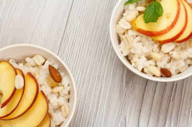 Sorghum lapalı porselen kaseler, şeftali, fındık, badem ve nane yaprakları gri ahşap tahtalarda. Taze meyveli vegan glütensiz sorghum salatası. Üst görünüm.