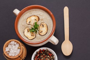 Porselen bir kasede dilimlenmiş mantar mantarlı krema çorbası, ahşap bir kaşık, tüm baharatlar ve siyah arka planda tuz bulunan küçük bir ahşap fıçı. Üst görünüm.