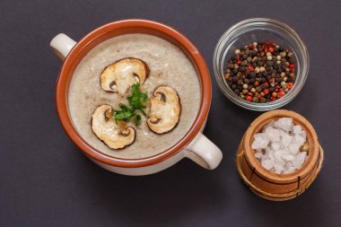 Porselen bir kasede dilimlenmiş mantar mantarlı krema çorbası, tüm baharatlar ve siyah arka planda tuz bulunan küçük bir ahşap fıçı. Üst görünüm.