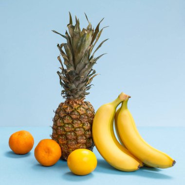 Tropikal meyvelerin doğal bileşimi. Taze ananas, muz, mavi arka planda bir limon ve portakal..