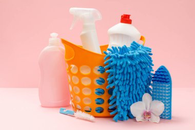 Plastik sepette bulaşık deterjanı, cam ve fayans temizleyicisi mikrodalga fırınlar ve fırınlar için deterjan pembe arka planda bez, fırça ve süngerler var. Yıkama ve temizleme seti.
