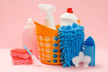Plastik sepette bulaşık deterjanı, cam ve fayans temizleyicisi mikrodalga fırınlar ve fırınlar için deterjan pembe arka planda bez, fırça ve süngerler var. Yıkama ve temizleme seti.