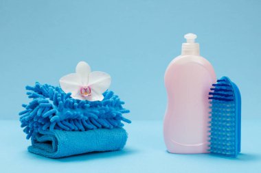 Plastik bulaşık deterjanı, paçavralar ve mavi arka planda bir fırça. Yıkama ve temizleme seti.