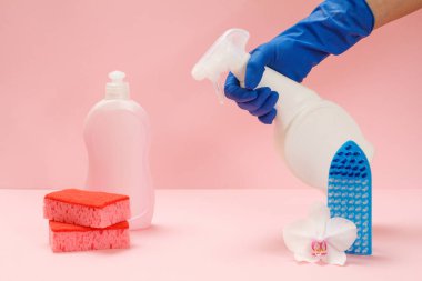Plastik bir şişe bulaşık deterjanı, sünger, fırça ve pembe arka planda cam ve fayans temizleyicisi tutan kauçuk bir eldiven. Yıkama ve temizleme seti.