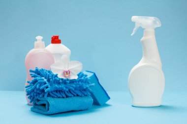 Plastik bulaşık deterjanı, cam ve fayans temizleyicisi, paçavralar ve mavi arka planda bir sünger. Yıkama ve temizleme seti.