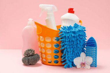 Plastik sepette bulaşık deterjanı, cam ve fayans temizleyicisi mikrodalga fırınlar ve fırınlar için deterjan, bez, fırça ve süngerler pembe arka planda. Yıkama ve temizleme seti.