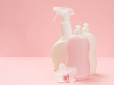 Plastik bulaşık deterjanı, cam ve fayans temizleyicisi mikrodalga fırınlar ve fırınlar için deterjan ve pembe arka planda beyaz bir orkide çiçeği. Yıkama ve temizleme seti.