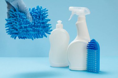 Mavi arka planda bir bez, çamaşır ve temizlik seti olan koruyucu eldivenli bir kadın eli..