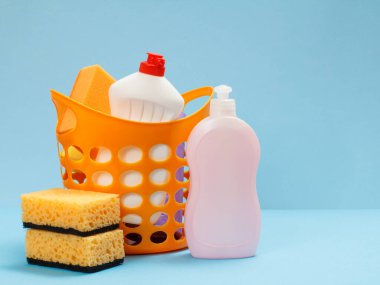 Mavi arka planda bulaşık deterjanı ve süngerli plastik sepet. Yıkama ve temizleme seti.